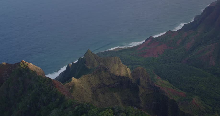 Waves hitting the shoreline at midday with a rugged mountain island lining the coast its slopes covered in green vegetation
