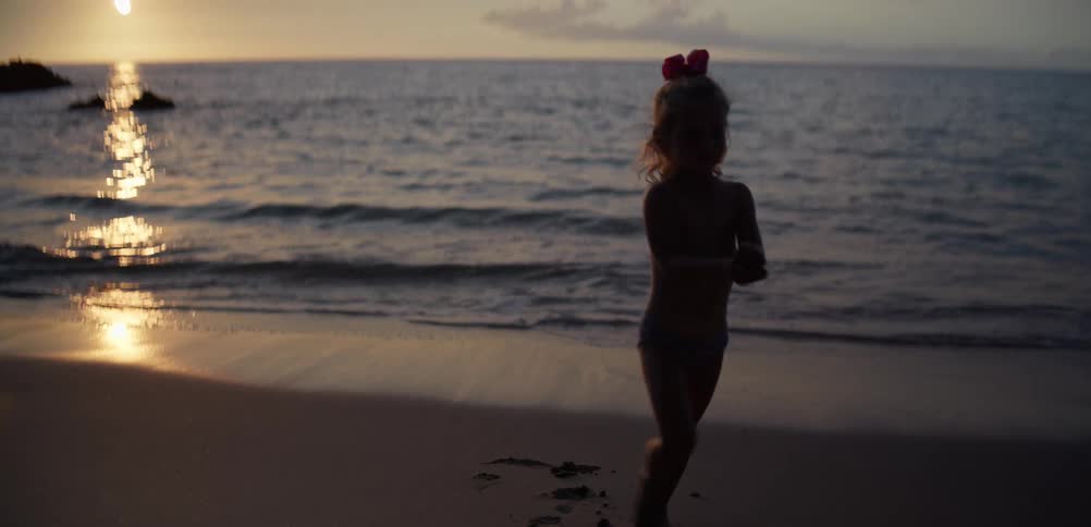 Girl playing on the beach carries sand as the sun sinks towards the horizon
