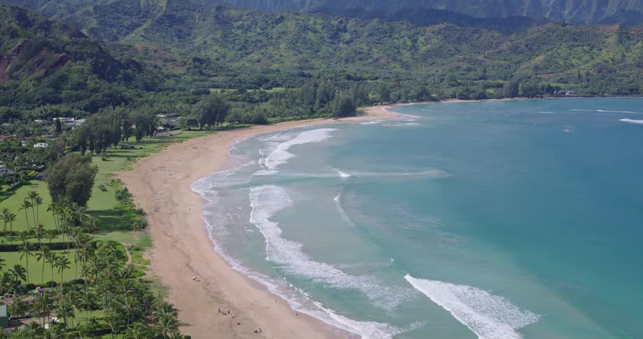 Aerial view of turquoise waves on a sandy tropical beach with green mountains beyond