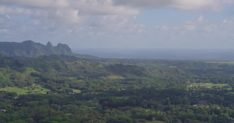 Tropical vegetation covers hills with rocky mountains in the background and ocean in the distance