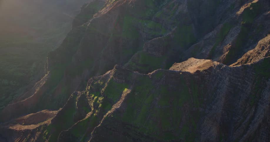 Sunlight glints off the steep green clad cliffs of a deep canyon as the camera glides along its rugged ridgeline