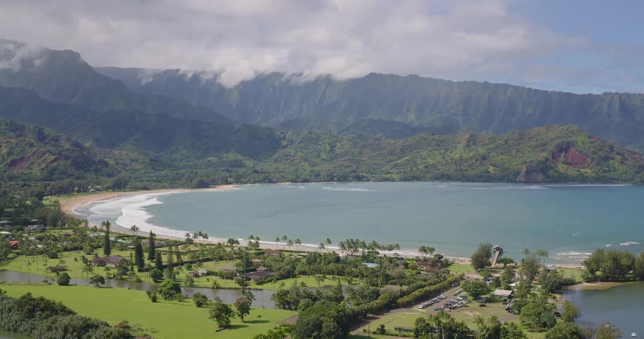 Tropical bay with turquoise waters bordered by beach palm trees buildings and cloudcovered mountains