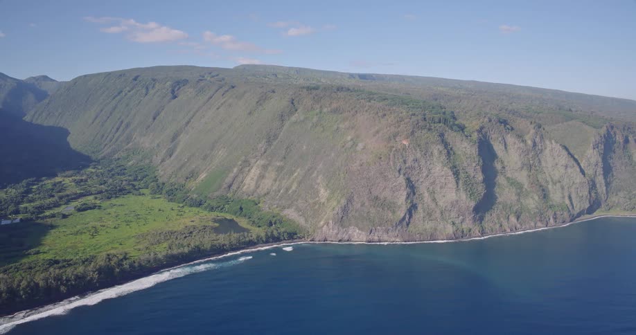 Aerial view of a rugged coastline with lush green hills meeting deep blue ocean waves crashing against the shore