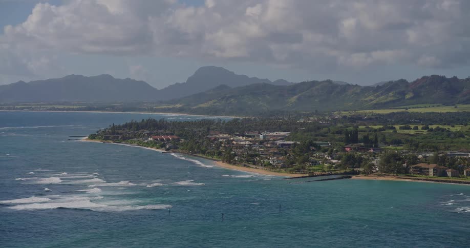 An ocean view at midday with a coastal town lining the shoreline and a mountain range rising in the background