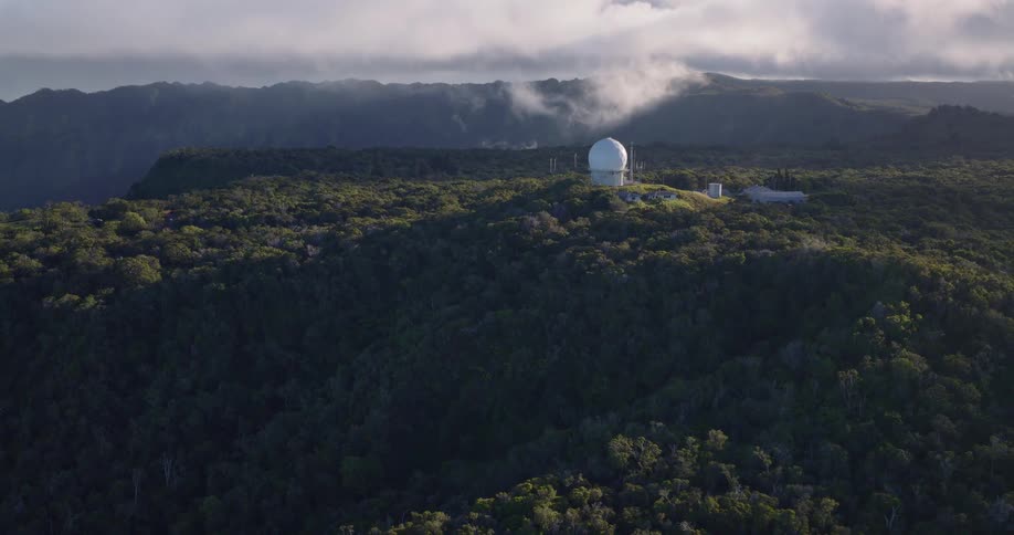 White radar dome rises atop forested hill surrounded by misty mountains and dense vegetation