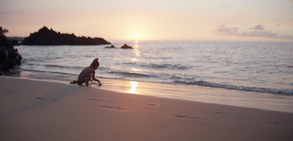 Little girl playing in the sand on the beach as waves roll in to shore