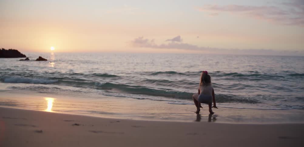Child runs along beach at sunset with golden reflection on sand and water