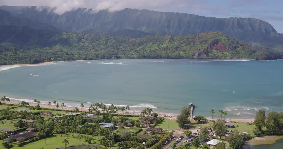 Tropical bay with calm waters is surrounded by green mountains palm trees and beachfront buildings