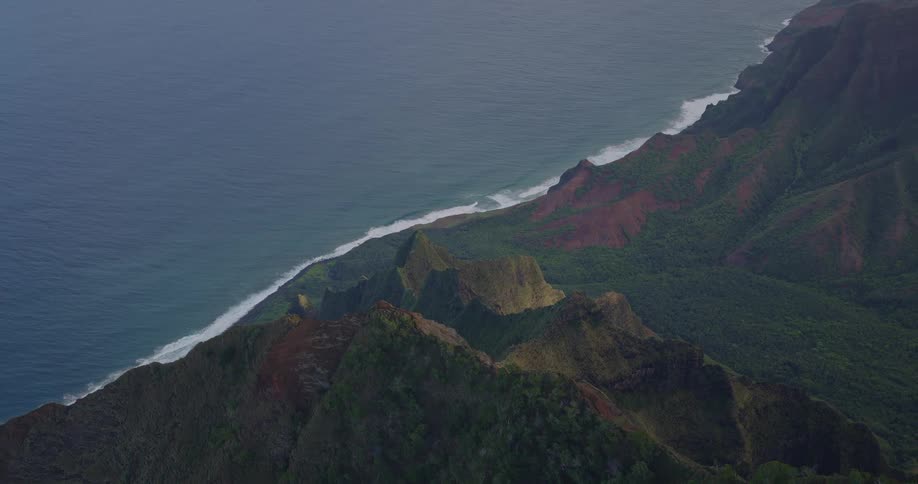 Waves hitting the shoreline at midday with a rugged mountain island lining the coast its slopes covered in green vegetation