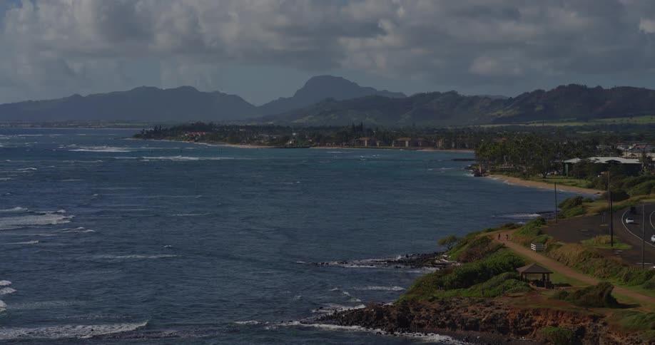 Coastline with an ocean road low cliffs vegetation and a mountain range in the background under a cloudy sky