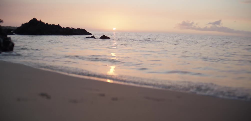 A quiet sandy beach with calm waves rolling onto the shore at sunset