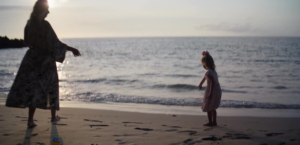 Woman and child standing on the sand looking toward the ocean at sunset