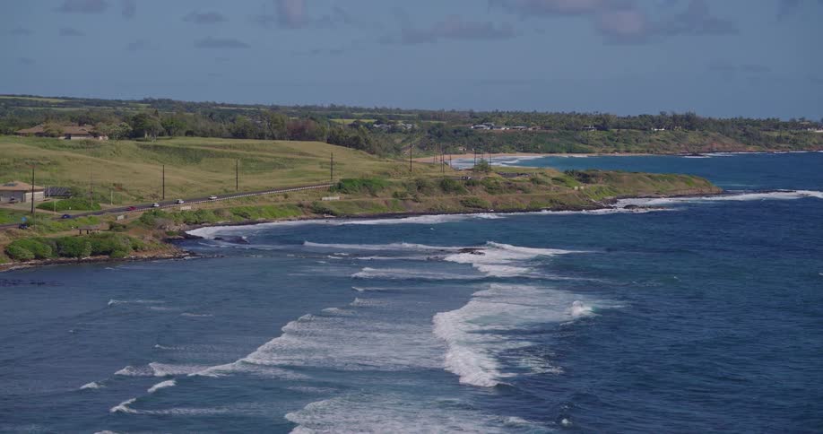 Jagged coastline with breaking waves and coastal road between green hills