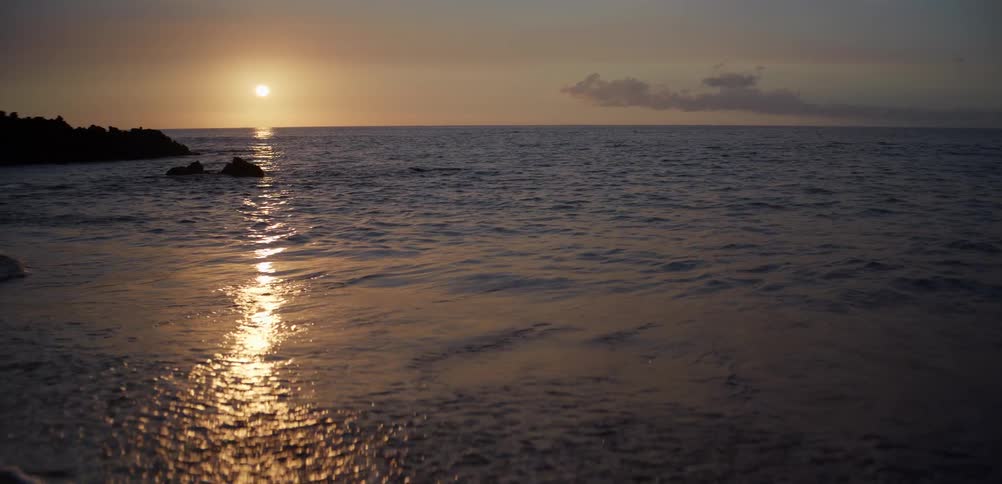 Peaceful sunset casts golden light over gentle ocean waves on a quiet sandy beach