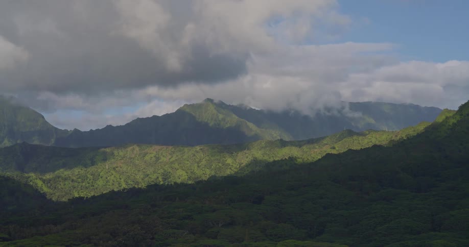Aerial view of lush green tropical mountains with drifting clouds under soft daylight