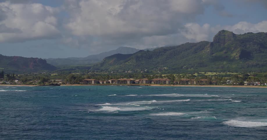 Coastal view with waves breaking in the sea a shoreline with aligned buildings and vegetationcovered mountains in the background