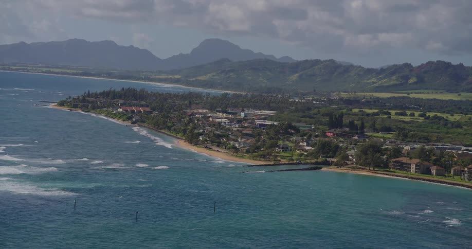 Coastal town surrounded by green mountains with curving beach and partly cloudy sky