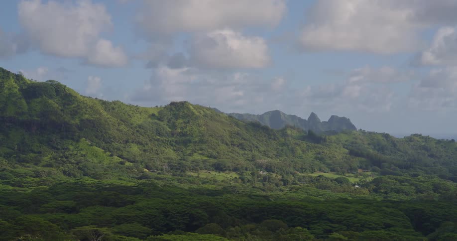 Green mountainous landscape under partly cloudy sky with dense vegetation and distant ocean view