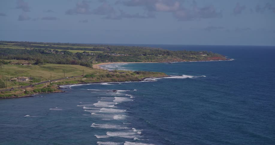 A coastline with a coastal road running along the shoreline at midday ocean waves crashing against the shore as cars move steadily along the busy road