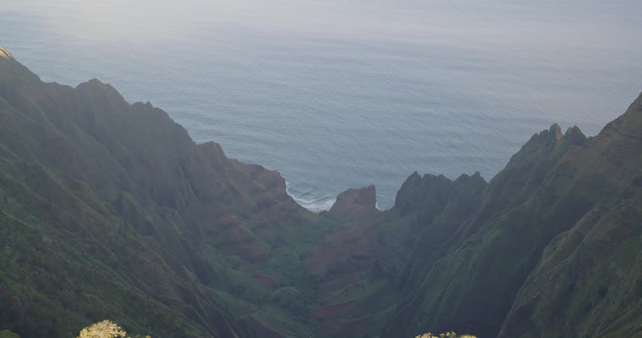 A rugged mountain range rising along the coastline at midday with the ocean stretching out in the background