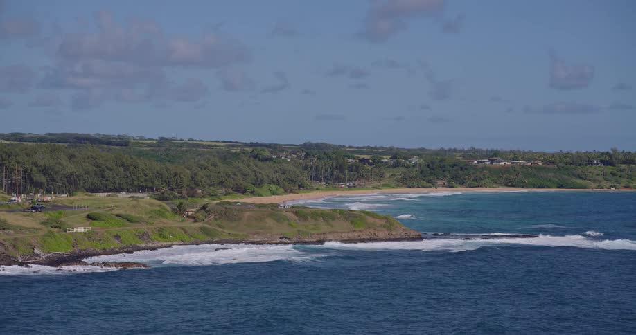 Aerial view of a tropical coastline with green hills meeting the deep blue ocean and rolling waves
