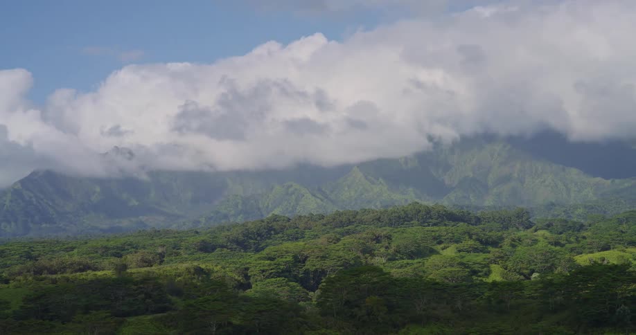 Lush tropical forest stretches toward cloudshrouded mountains beneath a partly blue sky