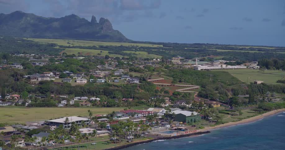 In the first video an aerial camera tilts upward from the deep blue ocean to reveal a massive lush green valley bordered by steep dramatic cliffs the second video provides a wide panning shot of a coastal town showing houses and buildings nestled bet