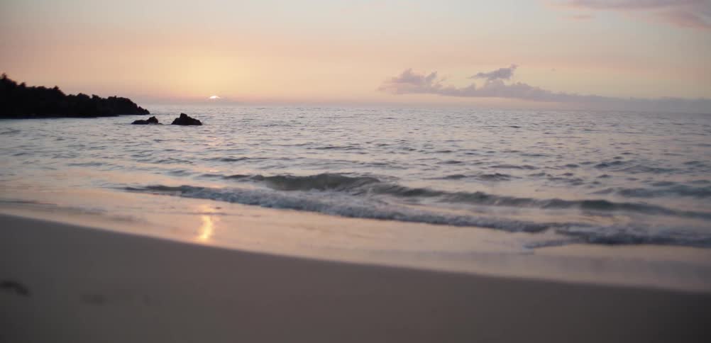 Waves roll in to shore and over the beach as sunlight reflects on the water