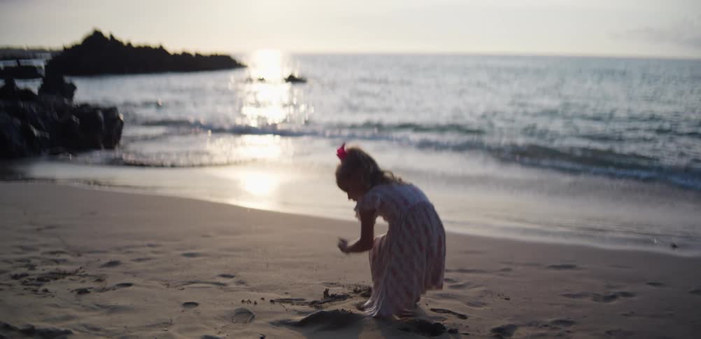 Child plays on the sand during sunset with gentle waves in the background