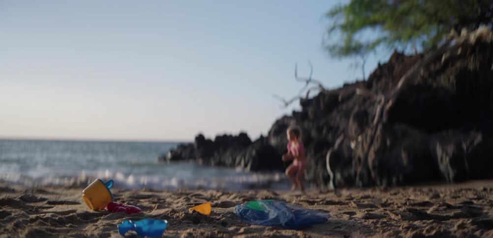 Little girl playing on the beach runs to the water near rocks and brings back a handful of wet sand