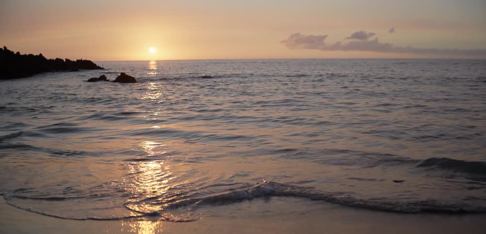 A beach at sunset ocean waves rolling onto the shoreline as the orange sun sinks in the distance
