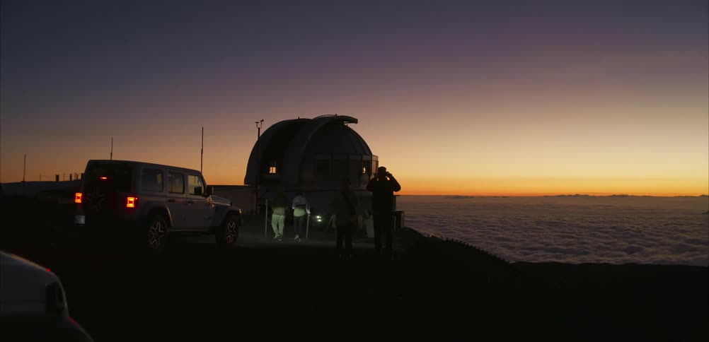 People gather near a dome observatory on a mountain ridge at sunset