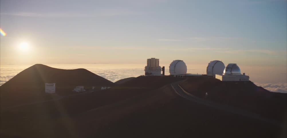 Astronomical observatories sit atop a mountain above the clouds under early morning light