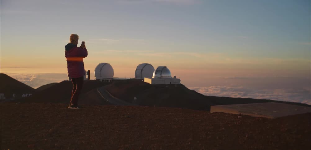 Person photographs the sunset near observatories on a mountain above the clouds