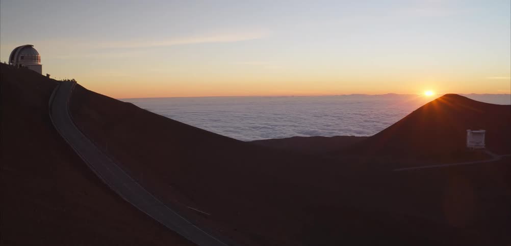 A astronomical observatories sit on a high mountain ridge above clouds at sunrise