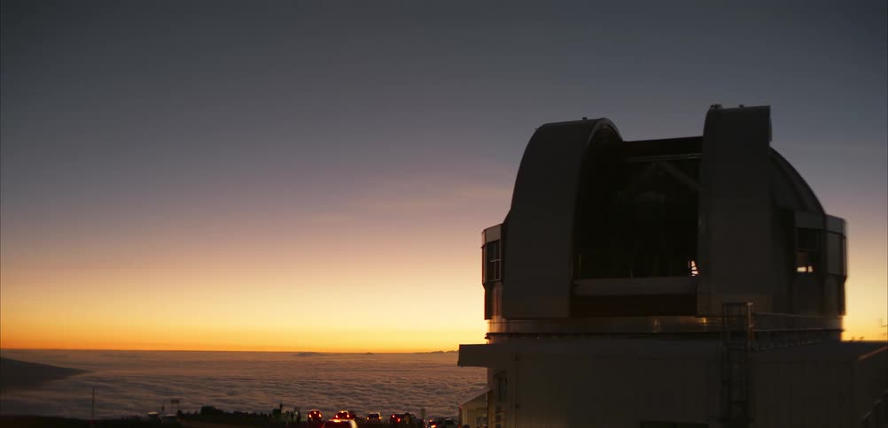 People walk by an observatory located on the coast while red tints the horizon