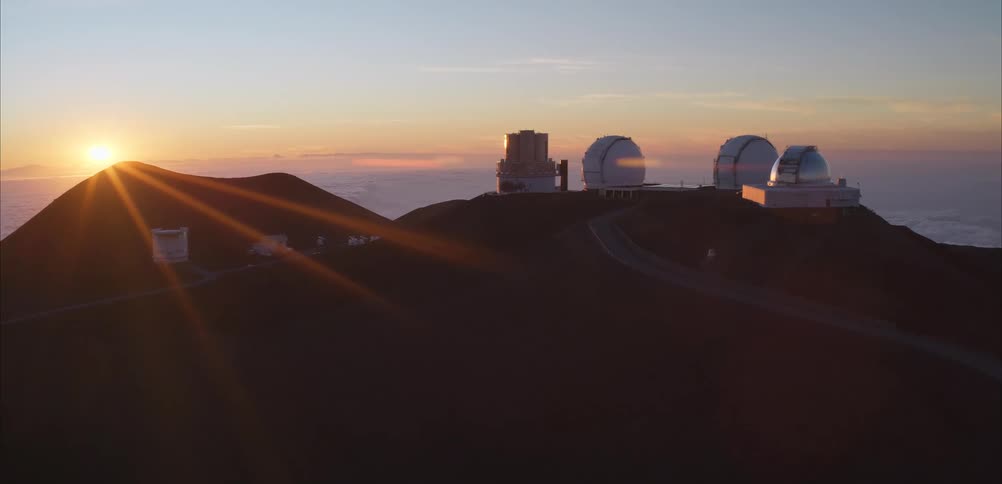 Observatory with multiple domes stands above clouds at sunset on mountain peak