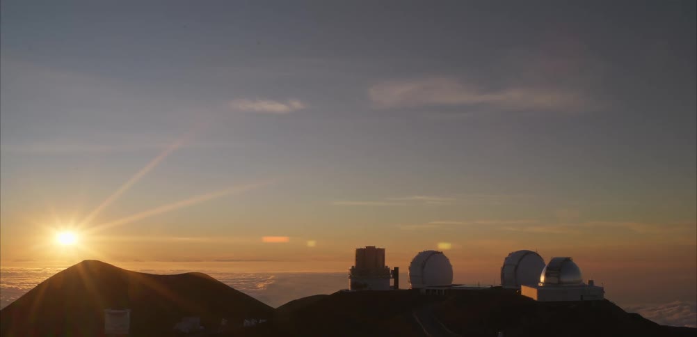 Observatory domes silhouette against golden sky at sunset on elevated mountain terrain