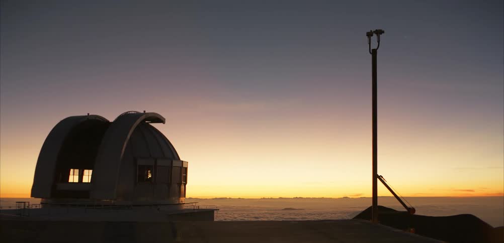 Observatory dome opens at dawn above clouds revealing telescope in elevated setting