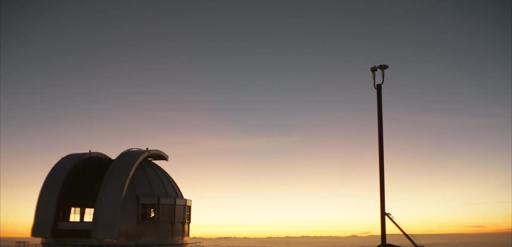 Observatory dome at dusk with a lit structure on the horizon and a gradientcolored sky