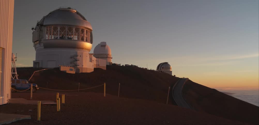 Astronomical observatories in white domes atop mountain at sunset with sky in orange and blue hues
