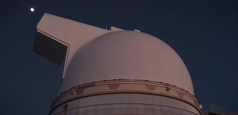 White observatory dome stands out under dark sky with moon visible in the background