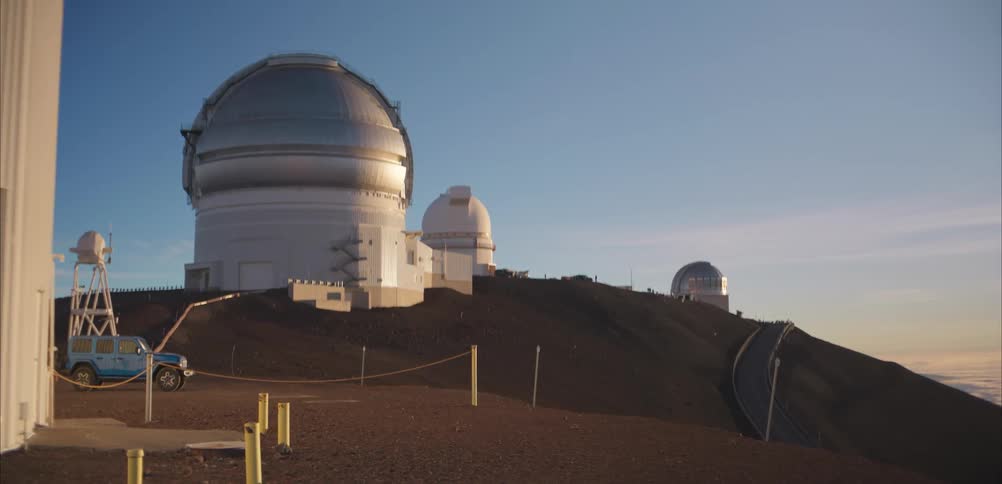 Large astronomical observatory domes sit on a barren mountain ridge under a clear sky
