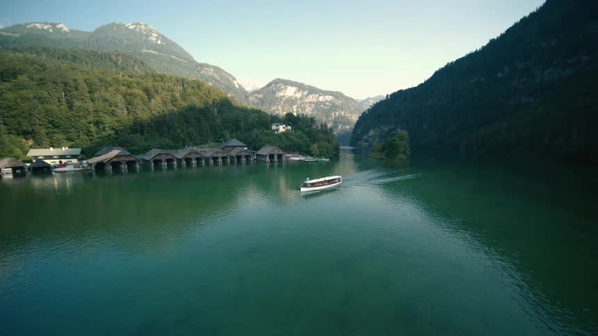 Boats glide across calm lake surrounded by snowy peaks and wooden houses along the shore