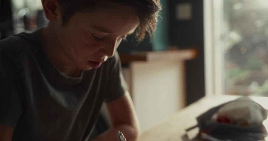 The sharp horizontal edge of the wooden table which creates a clear boundary between the boys focused workspace and the darker area in the foreground