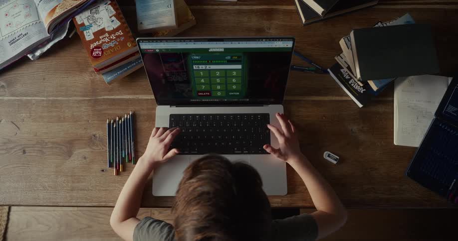 Little boy sitting at a table typing on the keyboard of a laptop computer using the calculator