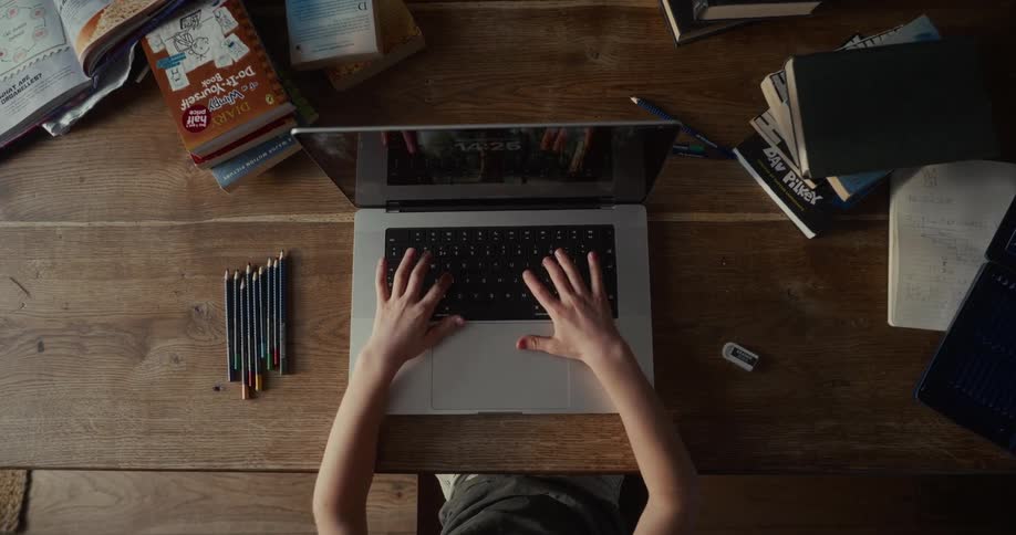 Little boy sitting at a table typing on the keyboard of a laptop computer