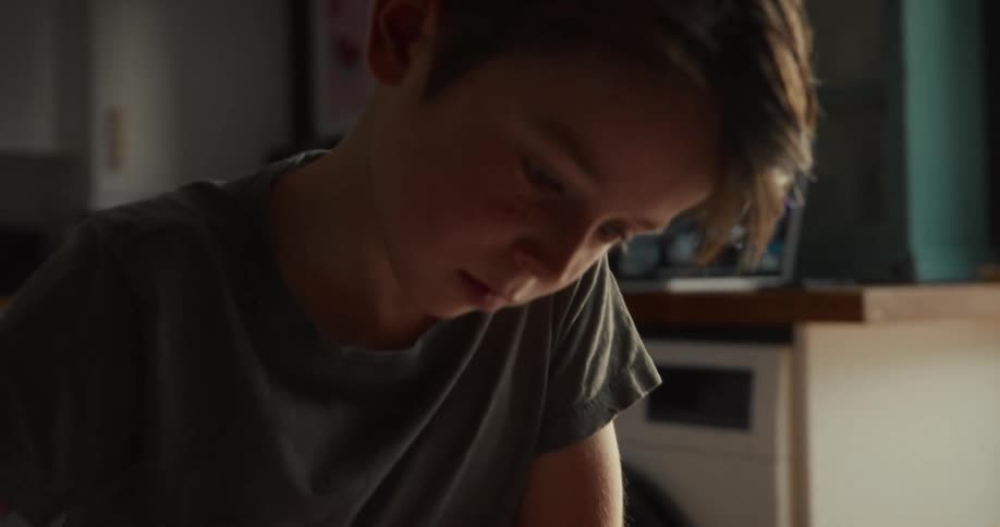 Young boy sitting on a chair scrathing a piece of paper with a pen over a wooden desk indoors during day time
