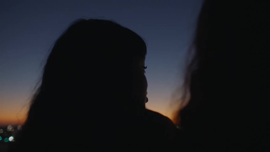 Two women watch over the city and talk at night