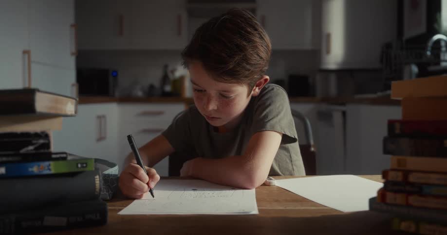 He horizontal edge of the wooden table which creates a sharp boundary between the boys drawing area and the lower foreground of the frame